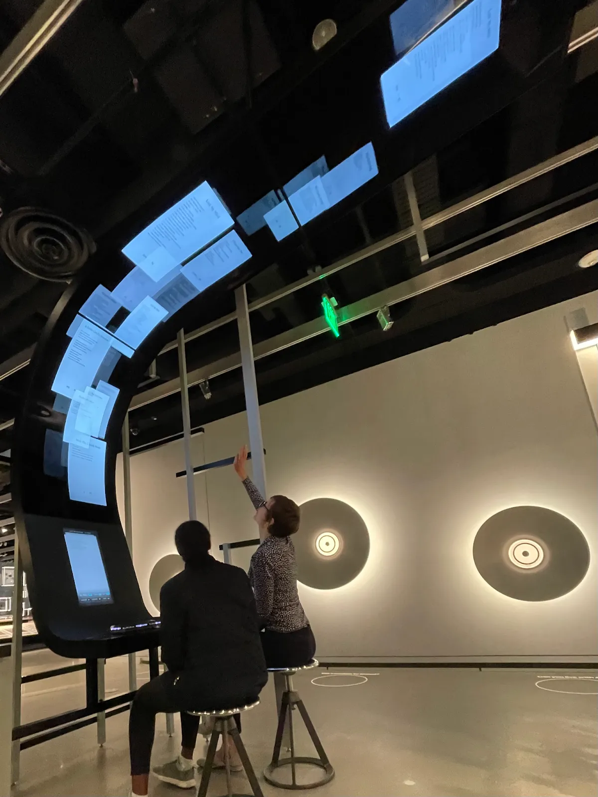 Visitors writing at the Collaborative Poetry station beneath a curved display of floating poems.